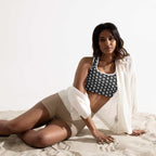 woman wearing muala workout fuel sports bra with pattern vol.1 design and beige shorts reclining on sand